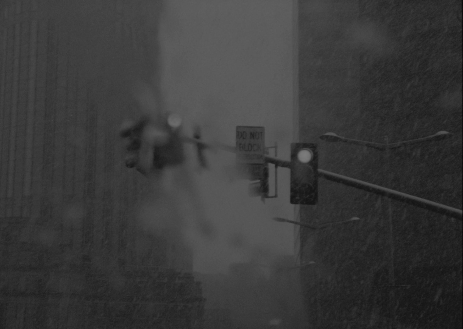 Snowy Boston intersection at night in black-and-white 16mm, with a Do Not Block sign, traffic light, and a blurred gesture, from I Woke Up in the Morning
